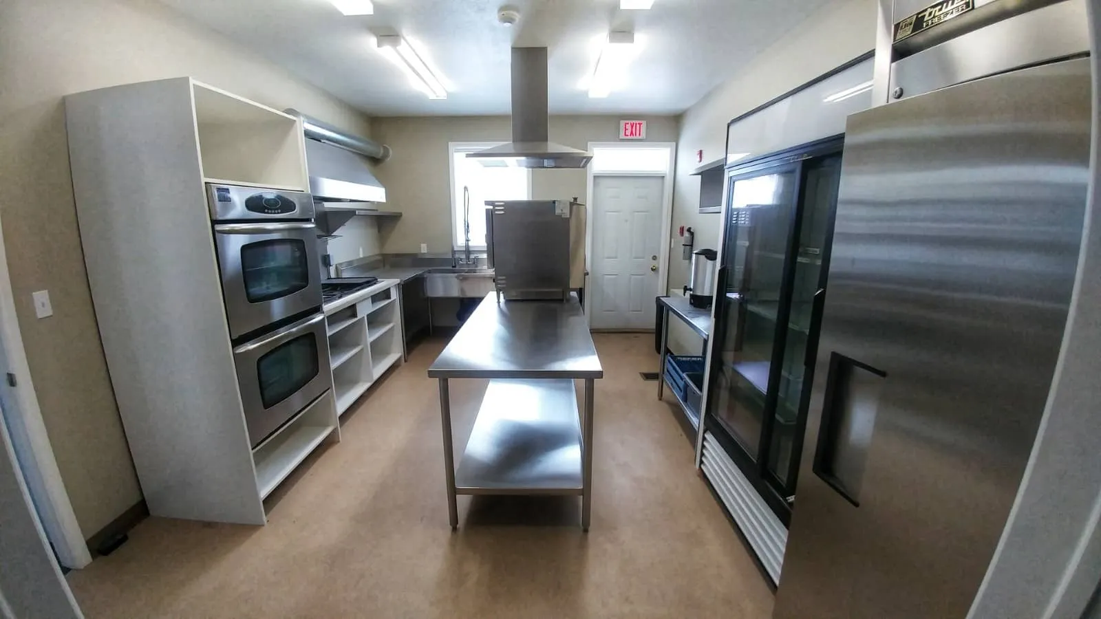 Commercial kitchen with stainless steel ovens, prep table and fridges